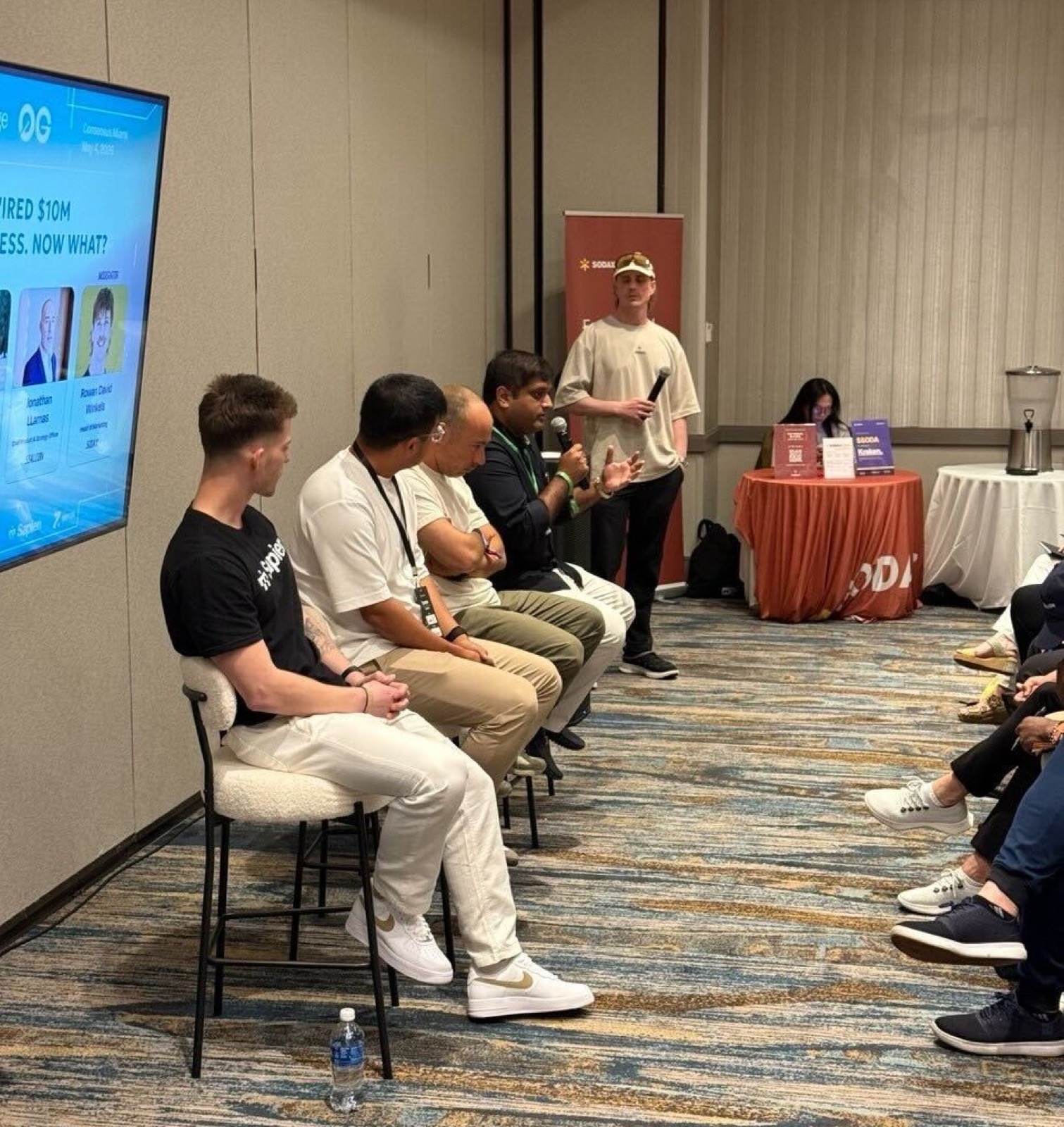 Wide-angle of the House of AI panel "Your agent just wired $10M to the wrong address. Now what?" with George V. on mic, 0G title slide on screen, at Miami Marriott Biscayne Bay