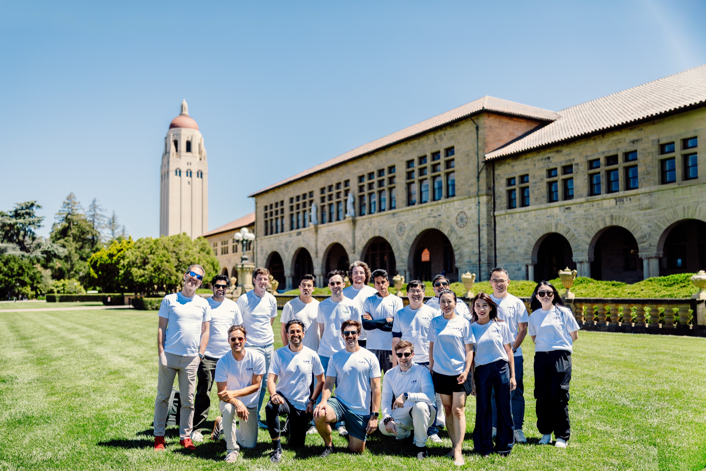 Seventeen people from the Apollo cohort and program team in white Apollo T-shirts on Stanford's Main Quad with Hoover Tower behind