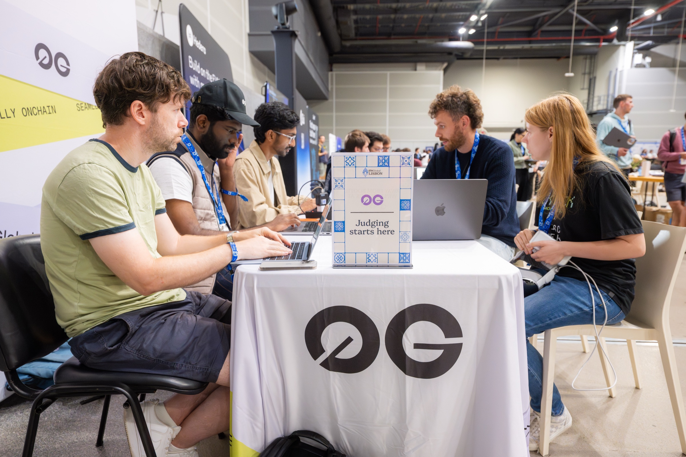 Builders demoing to 0G judges at the 0G table with a Judging starts here sign